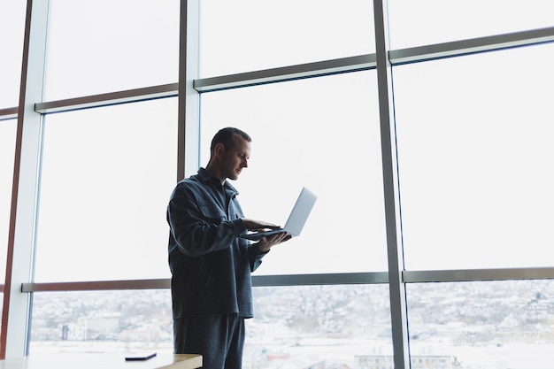 Homem de negócios jovem segurando um telefone em um escritório ou centro de negócios no contexto de grandes janelas de um arranha-céu Conceito de trabalho e carreira