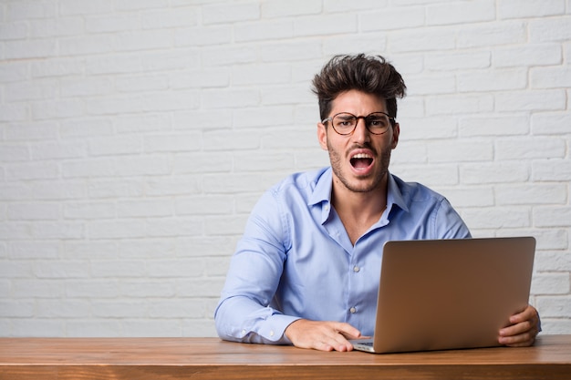 Foto homem de negócios jovem sentado e trabalhando em um laptop muito irritado e chateado