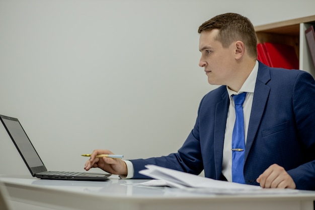 Homem de negócios jovem trabalhando em casa com o laptop e papéis na mesa.