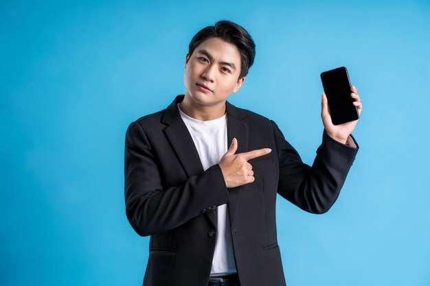 Homem de negócios jovem vestindo um colete usando telefone e posando em um fundo azul