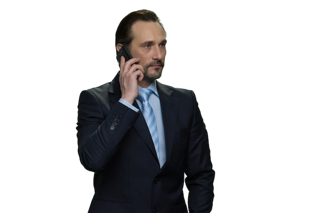 Homem de negócios maduro sério ligando com o telefone celular. Isolado na parede branca