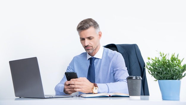 Homem de negócios maduro trabalhando no escritório com blog de negócios de smartphone e laptop