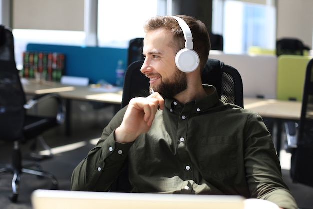 Homem de negócios moderno feliz trabalhando usando laptop enquanto está sentado no escritório.