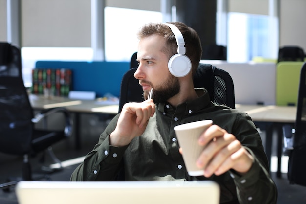 Homem de negócios moderno jovem sentado no escritório e segurando o copo de papel.