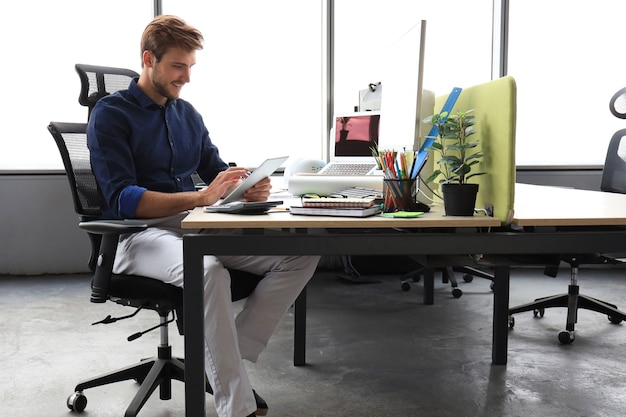 Homem de negócios moderno jovem trabalhando usando tablet digital enquanto está sentado no escritório.