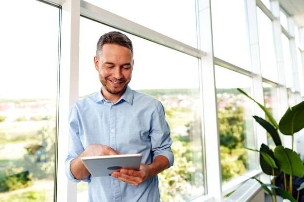 Homem de negócios moderno usando tablet digital enquanto estava perto da janela em seu escritório