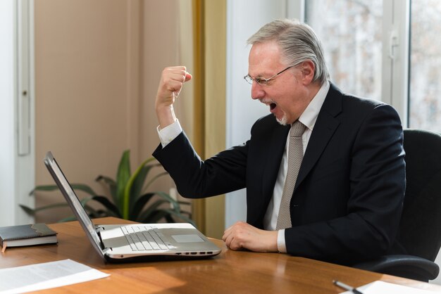 Homem de negócios muito feliz na frente de seu laptop no escritório