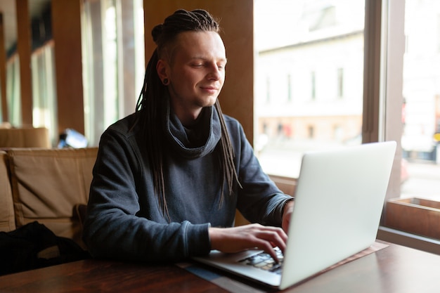 Homem de negócios novo com o dreadlock que faz seu trabalho no café com portátil.