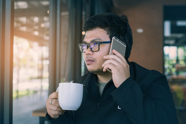 Homem de negócios novo que chama o telefone celular e que trabalha na loja do café.