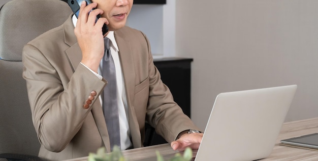 Homem de negócios que fala no smartphone e que trabalha no laptop na mesa de escritório