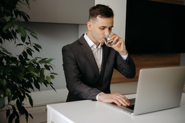 Homem de negócios que trabalha no homem de negócios do computador portátil bebendo um copo de água no escritório