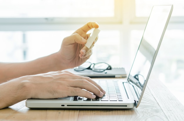 Homem de negócios que usa o computador com um cartão de crédito para comprar on-line.