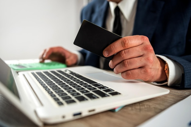 Homem de negócios segurando cartão de crédito para compras on-line usando laptop