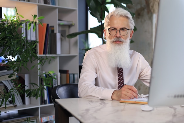 Homem de negócios sênior com uma barba estilosa, trabalhando no computador em sua mesa de escritório.