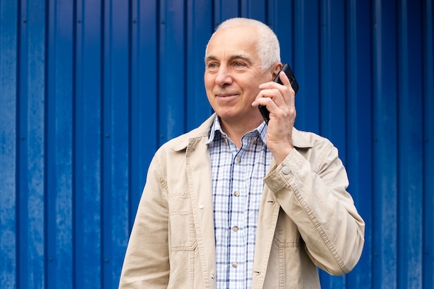 Homem de negócios sênior falando com o smartphone em fundo azul, copyspace. Homem sênior, tecnologia moderna