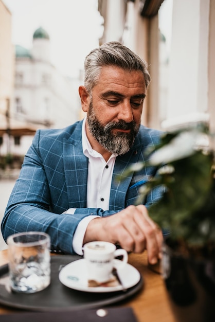 Homem de negócios sênior moderno fuma um cigarro enquanto descansa em um café depois de um árduo dia de trabalho