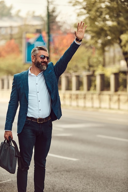 Homem de negócios sênior moderno parando um táxi na cidade.