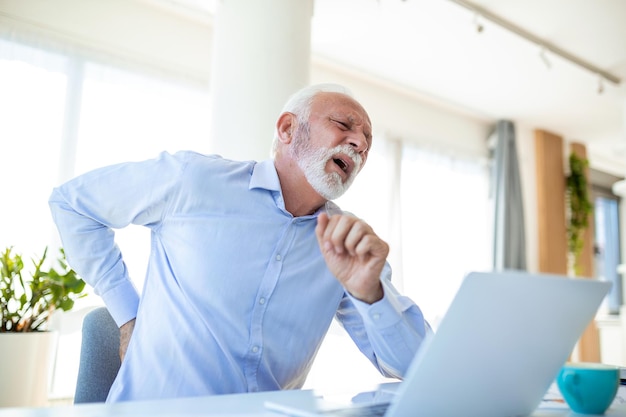 Homem de negócios sênior trabalhando sentado na mesa sofre de dor lombar Danos nos discos intervertebrais articulações espinhais compressão de raízes nervosas causadas por postura errada e trabalho sedentário