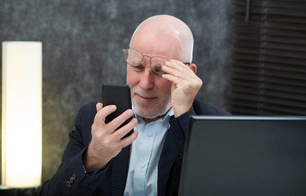 Homem de negócios sênior usando smartphone, ele está tendo dificuldades e problemas de visão