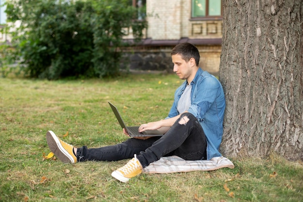 Homem de negócios sente-se no gramado trabalhar ao ar livre no computador em um parque.