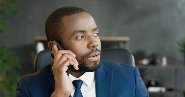 Homem de negócios sério afro-americano falando no smartphone. Macho tendo conversa de celular.