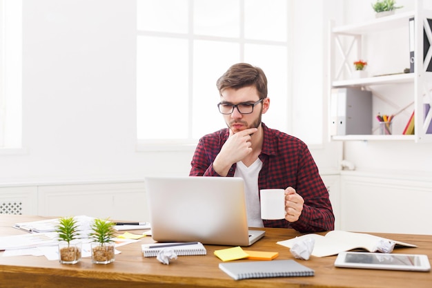 Homem de negócios sério no escritório. Empregado casual jovem pensativo no trabalho com o computador, o conceito de problemas de trabalho. Retrato de estilo de vida