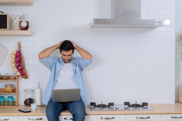 Homem de negócios sério trabalhando em casa tendo problemas com o pensamento de trabalho para resolver o problema Homem bonito usando um laptop na cozinha