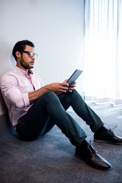 Homem de negócios sério usando computador tablet enquanto está sentado no chão