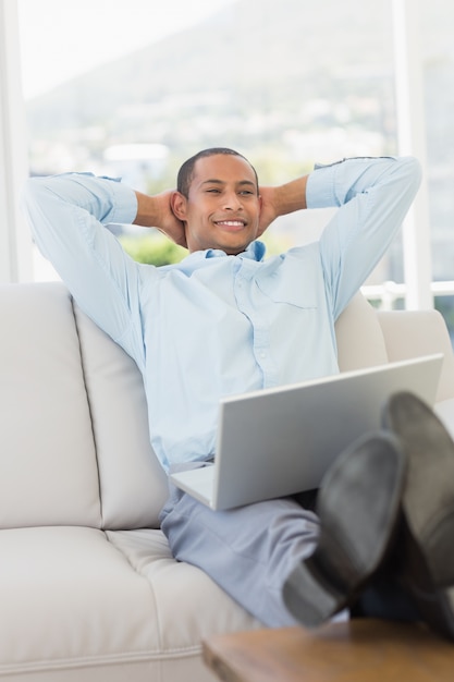 Homem de negócios sorridente relaxado no sofá com laptop