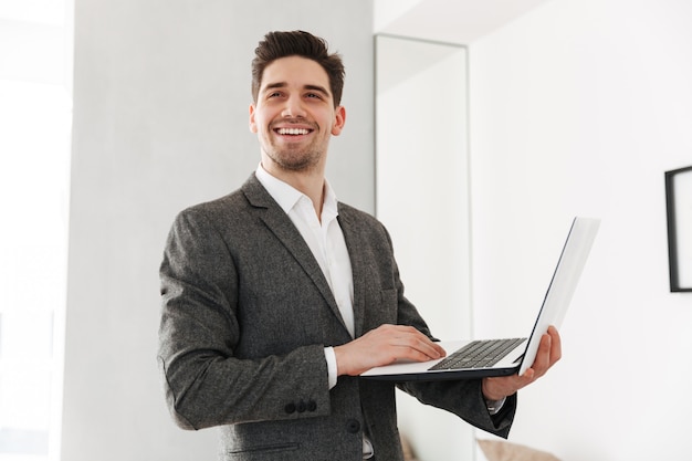 Homem de negócios sorridente segurando o laptop enquanto olhando para longe