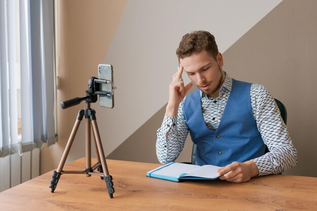 Homem de negócios sorridente usando telefone e tripé fazendo videochamada para colegas de trabalho