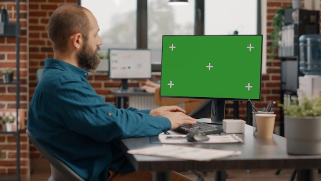 Homem de negócios trabalhando com tela verde horizontal no monitor no escritório. Empregado usando fundo isolado e modelo de maquete com chroma key na tela do computador. Adulto com tecnologia