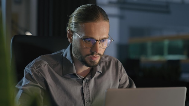 Homem de negócios trabalhando horas extras gerente à noite à noite trabalho de escritório escuro com laptop sério