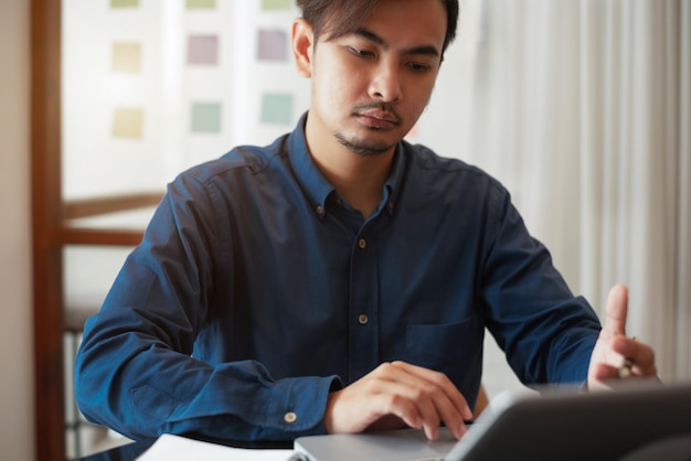 Homem de negócios trabalhando no computador portátil procurando e anotando no caderno de papel com caneta trabalhando no escritório