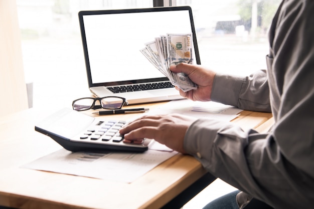 Homem de negócios usando a calculadora e segurando o dinheiro