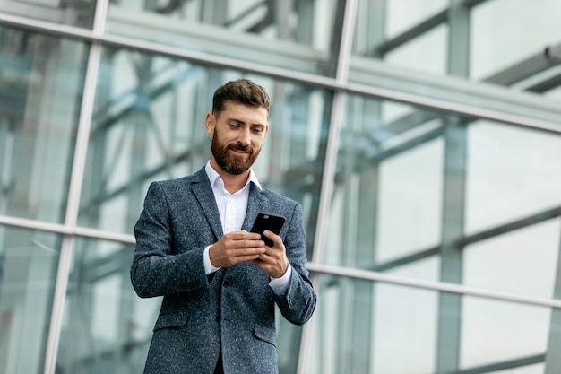 Homem de negócios usando smartphone e sorrindo no aeroporto. Executivo empresarial novo com telefone móvel no aeroporto.