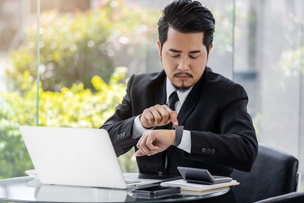 Homem de negócios, verificando o tempo no relógio inteligente enquanto estiver usando o laptop