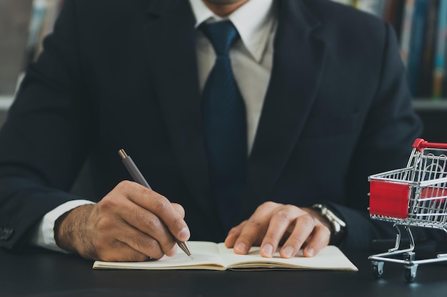 Homem de negócios vestindo terno e calcula o orçamento Carrinho de compras na mesa com notebook Orçamento da família pobre de baixa renda Aumento dos preços dos alimentos e mercearias e bens de consumo diários caros