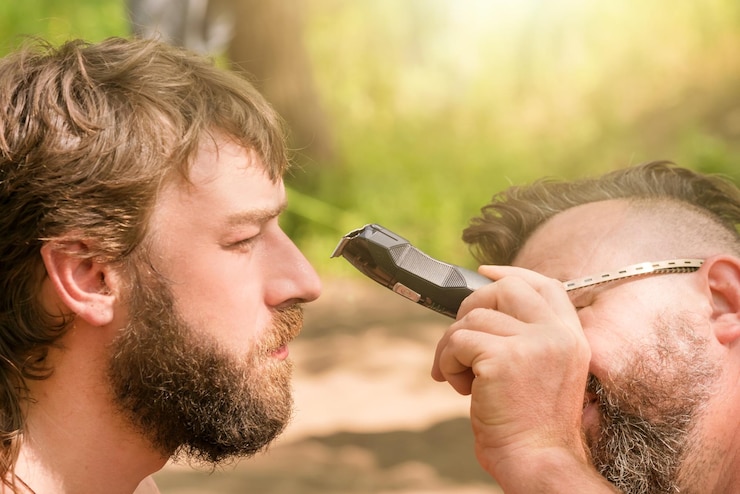 Foto homem de óculos corta a barba do outro homem usando máquina de cortar cabelo