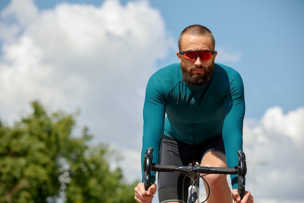 Homem de óculos de sol acelera ao longo da estrada contra o fundo do parque de verão Homem com um hobby de bicicleta anda no parque