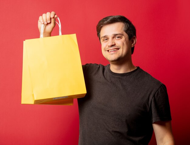 Foto homem de óculos e camiseta com sacola de compras no espaço vermelho