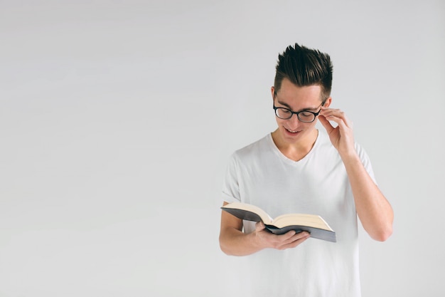 Homem de óculos e uma camiseta branca está lendo um livro sobre um fundo branco