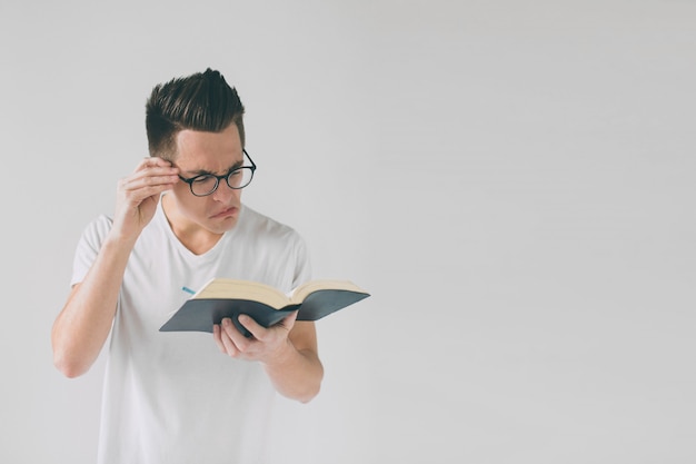 Homem de óculos e uma camiseta branca está lendo um livro sobre um fundo branco