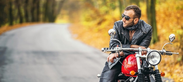 Homem de óculos escuros e jaqueta de couro sentado em uma motocicleta na estrada