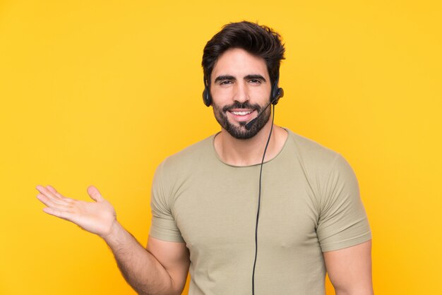 Homem de operador de telemarketing trabalhando com um fone de ouvido sobre parede amarela isolada segurando copyspace imaginário na palma da mão