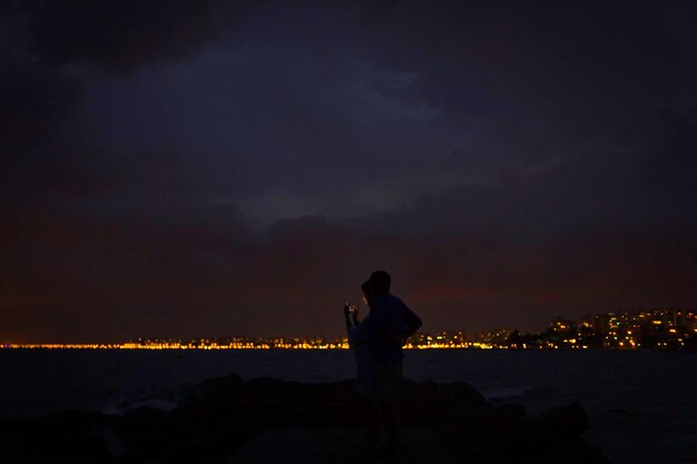 Homem de pé ao lado do mar contra o céu à noite