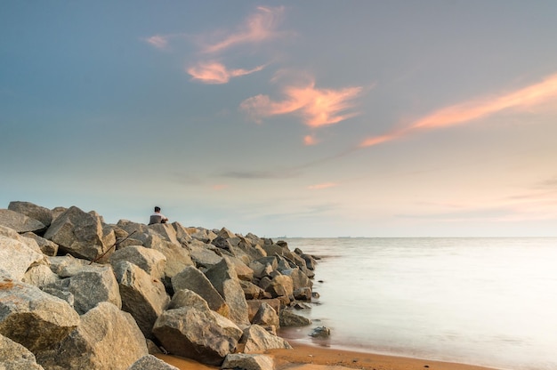 Homem de pé em uma rocha ao lado do mar contra o céu durante o pôr do sol