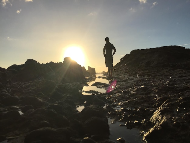 Foto homem de pé junto ao mar contra o céu durante o pôr-do-sol