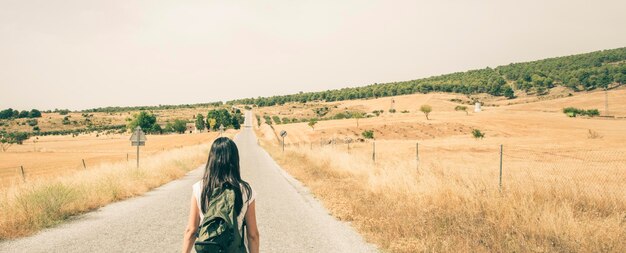 Homem de pé na estrada no meio do campo contra o céu claro