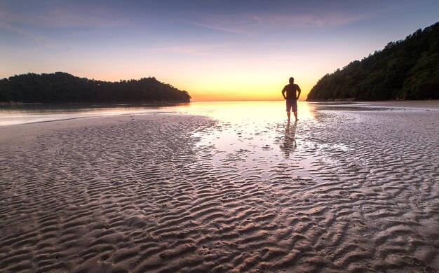 Foto homem de pé na praia contra o céu durante o pôr do sol